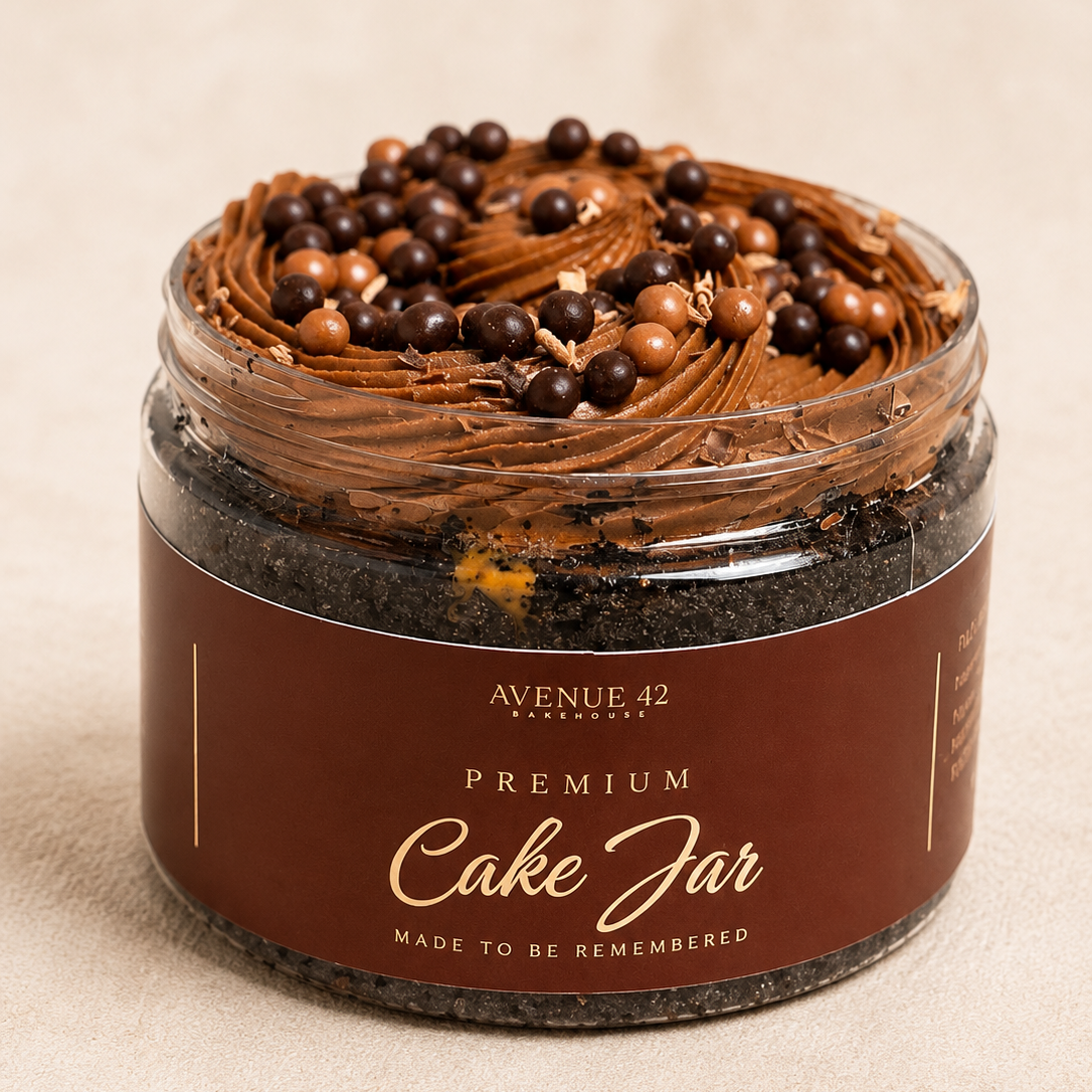 A premium chocolate cake jar by Avenue 42, featuring a rich chocolate frosting topped with chocolate shavings, chocolate chips, and cookie crumbs, in a clear jar with a dark brown label.
