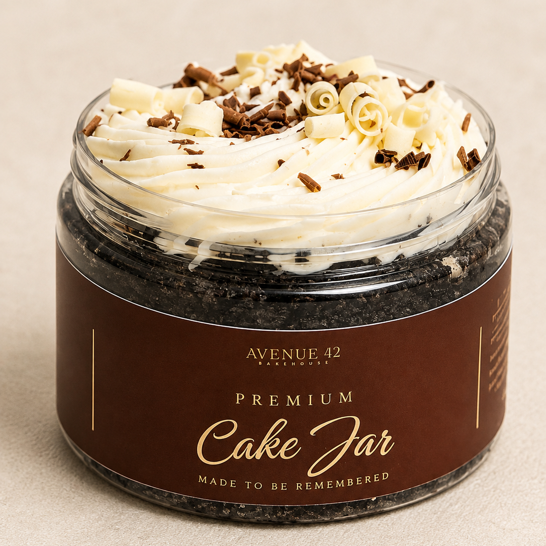 A gourmet chocolate cake jar by Avenue 42, featuring a dark chocolate cake base, piped white cream on top with chocolate curls and shavings, and a brown label with cream lettering.