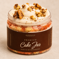 A jar filled with a layered carrot cake, topped with buttercream and chopped walnuts, wrapped in a dark brown label that reads 'PREMIUM Cake Jar' by Avenue 42 Bakery.