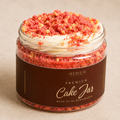 A clear jar filled with a layered strawberry cake-like treat, topped with white cream and pink-orange crumb topping, with a dark brown label reading Avenue 42 Premium Cake Jar.
